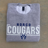 Folded gray sweatshirt with 'Norco Cougars' text and logo on a brown surface